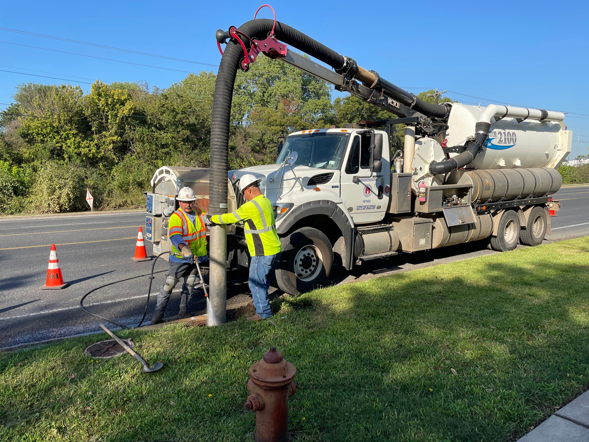 two individuals are cleaning a large pipe on the side of the road